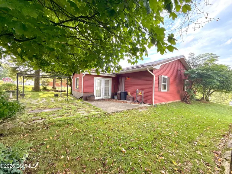 Back of the house with red siding, French doors to a patio and stone-paved yard area