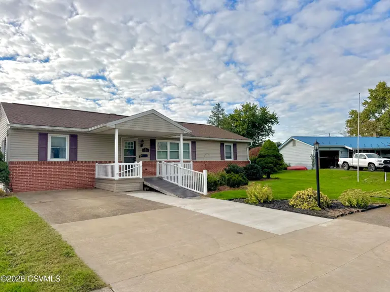 Ranch home and concrete driveway with a white-railed ramp leading to the covered porch