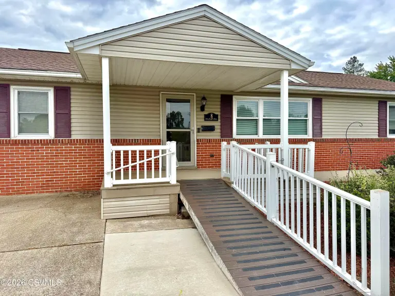 Covered front porch with white railings, a ramp and the front door